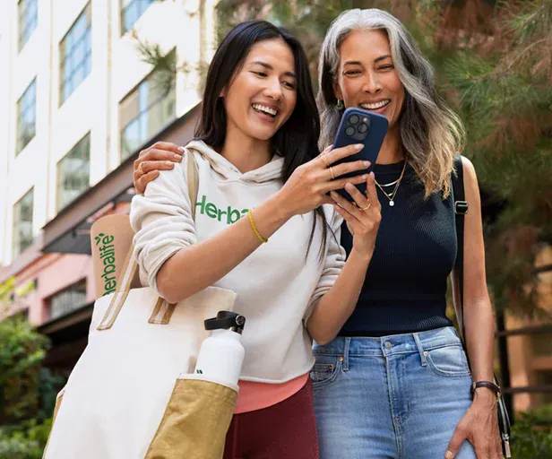 Dos mujeres sonriendo mirando un móvil, con ropa y accesorios Herbalife